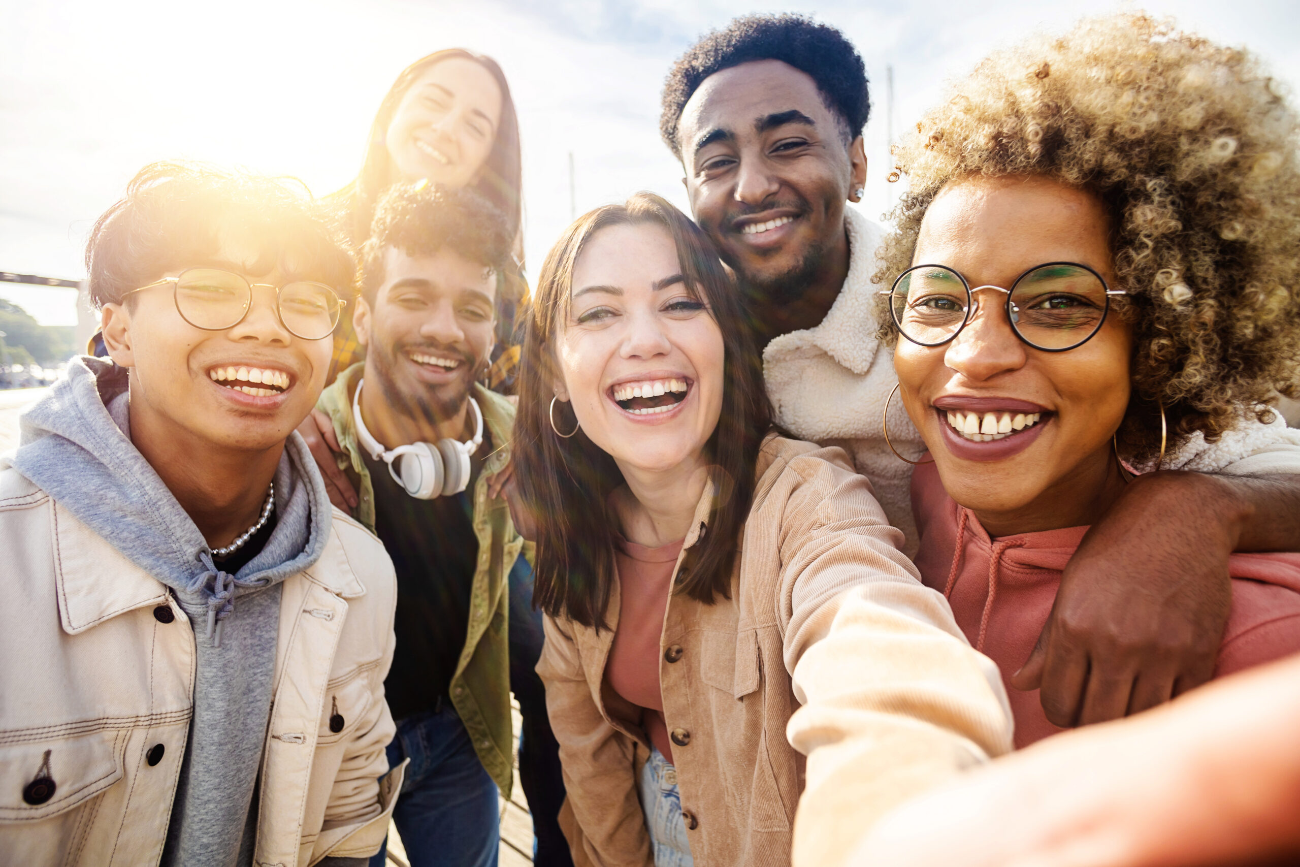 Happy young friends having fun while taking a selfie with mobile phone outdoors United group of happy young friends having fun while taking a selfie with mobile phone outdoors - Diverse group of millennial people laughing together during vacation - Friendship and holidays concept