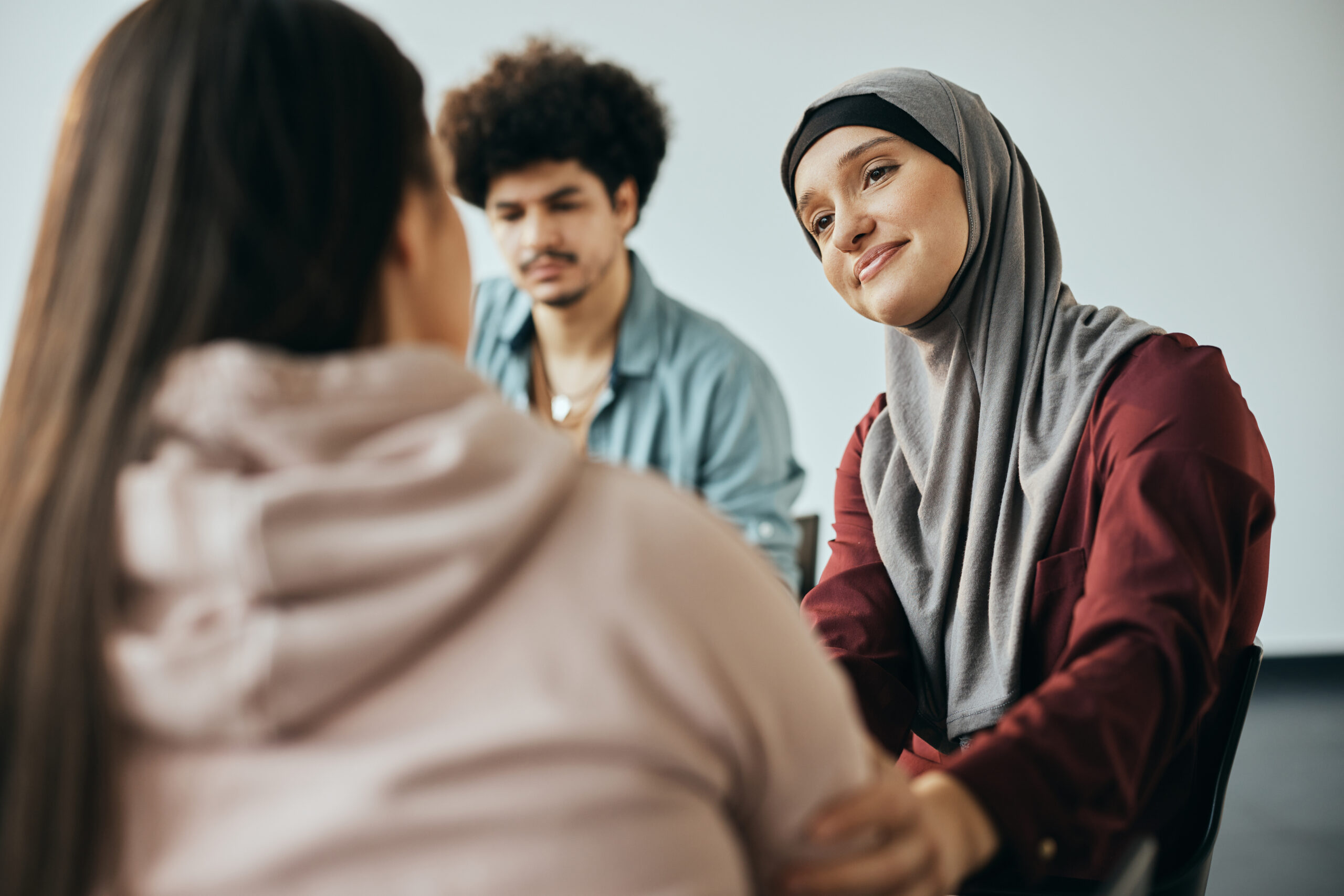 Muslim woman supporting new attender of group therapy to talk about herself during meeting at mental health center. Muslim woman supporting new attender of group therapy to talk about herself during meeting at mental health center.