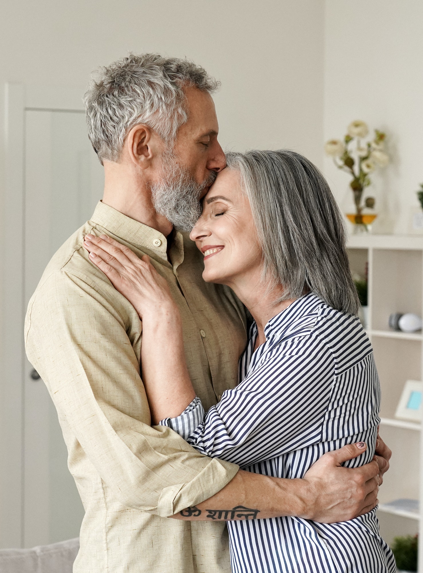 Smiling mid age older couple hugging and kissing standing at home. Smiling mid age older couple hugging and kissing standing at home.
