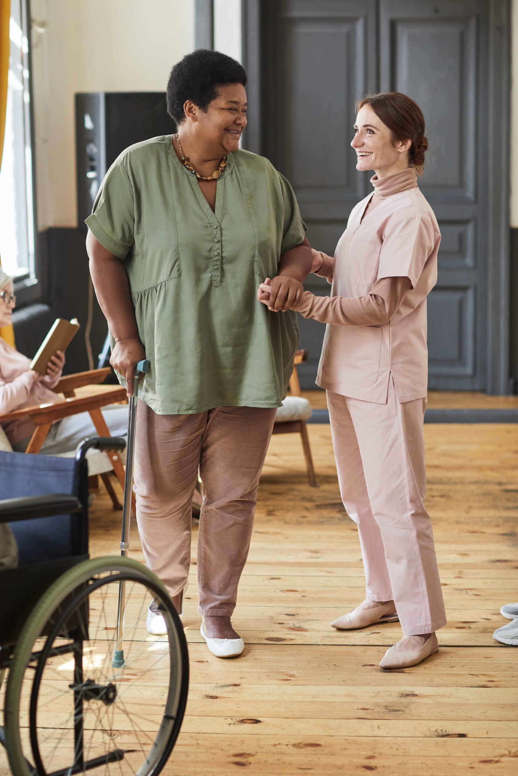 Caring Nurse Helping Senior Woman in Retirement Home Vertical full length portrait of smiling young woman helping seniors in modern retirement home
