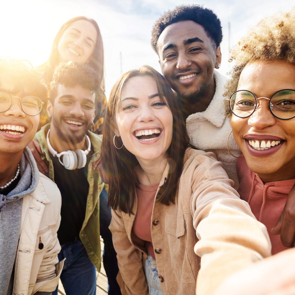 United group of happy young friends having fun while taking a selfie with mobile phone outdoors - Diverse group of millennial people laughing together during vacation - Friendship and holidays concept