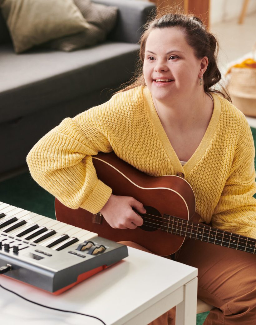 Modern young Caucasian woman with Down syndrome spending time at home enjoying playing guitar